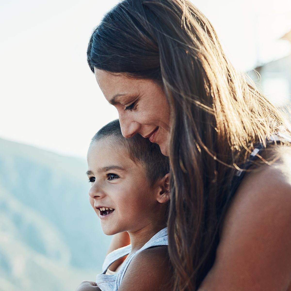 A mother holding her young child outdoors in warm sunlight.
